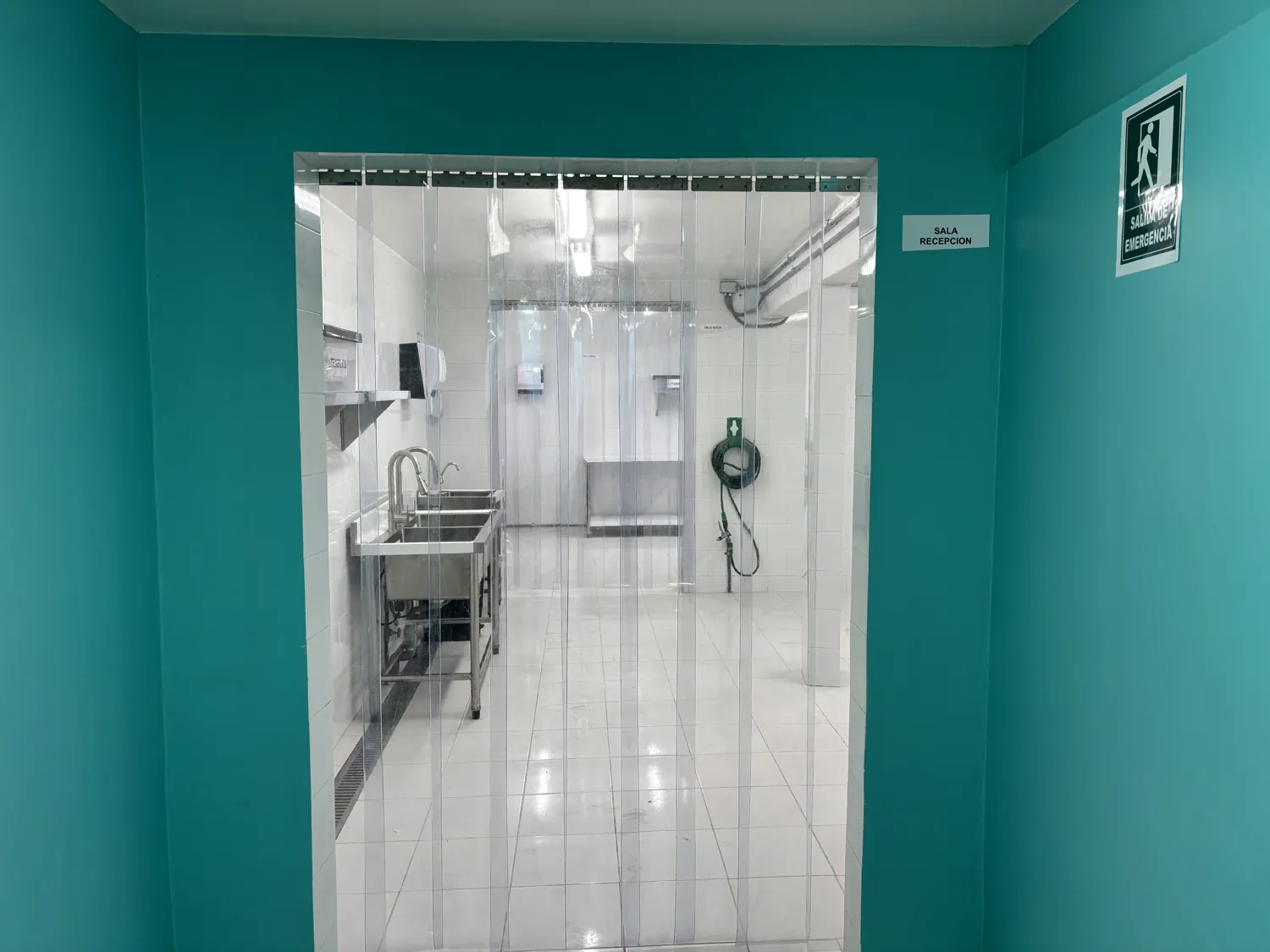 Sala de recepción de la planta, con cortina sanitaria de PVC y lavamanos de acero inoxidable